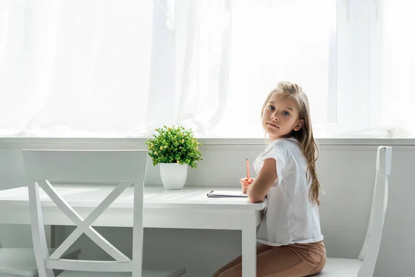 Cute kid sitting and holding pencil near notebook at home — Stock Photo