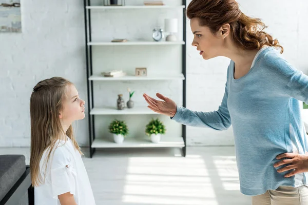 Frustrated mother standing with hand on hip and gesturing near daughter — Stock Photo