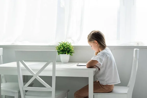 Cute kid sitting and writing in notebook at home — Stock Photo