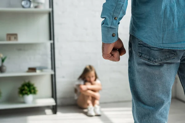 Selective focus of angry man threatening with fist while standing near scared kid sitting on floor — Stock Photo