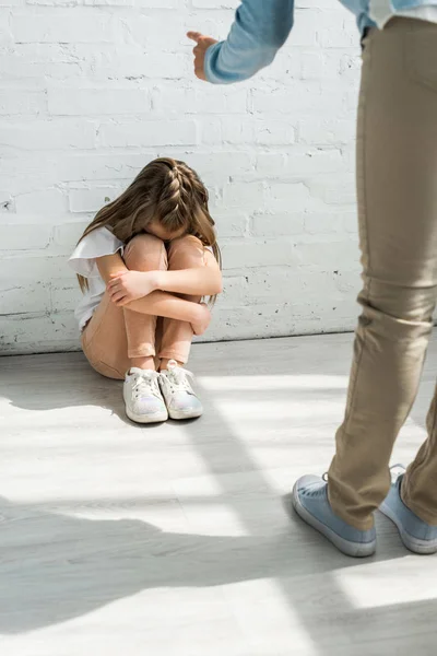 Ausgeschnittene Ansicht der Mutter, die mit dem Finger auf aufgebrachte Tochter zeigt, die zu Hause auf dem Boden sitzt — Stockfoto