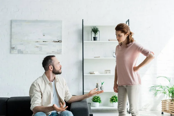 Upset man gesturing while looking at woman standing with hand on hip — Stock Photo