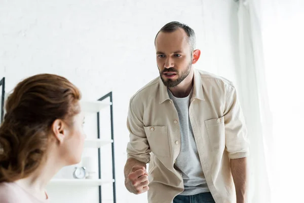 Enfoque selectivo de hombre enojado mostrando puño mientras mira a la esposa en casa - foto de stock