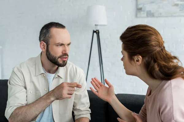 Selective focus of handsome man pointing with finger at woman at home — Stock Photo