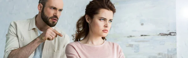 Panoramic shot of handsome man pointing with finger at upset woman — Stock Photo