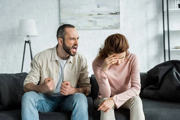 Homme en colère assis sur le canapé et criant à femme bouleversée — Photo de stock