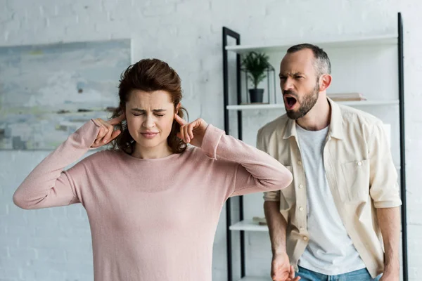 Selective focus of woman with closed eyes covering ears near screaming man — Stock Photo