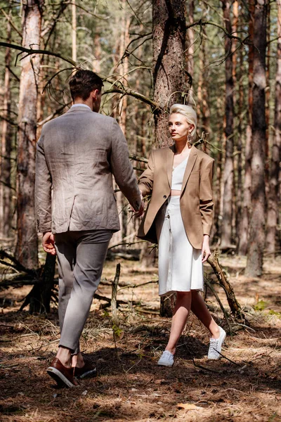 Vue arrière de l'homme et de la femme se tenant la main l'un devant l'autre dans la forêt — Photo de stock