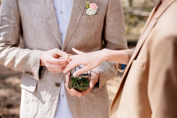 Cropped view of bridegroom and bride putting wedding ring on finger — Stock Photo