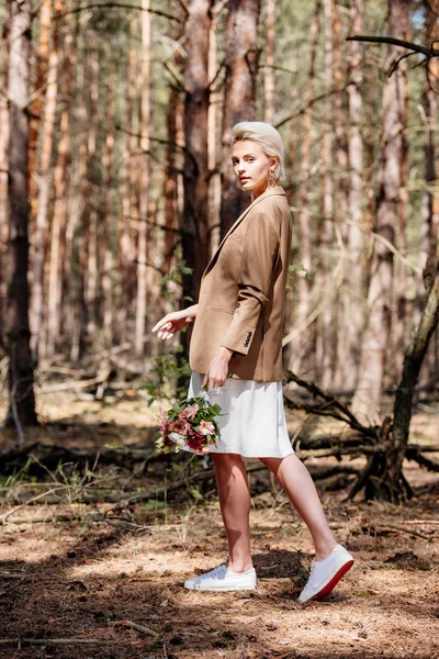 Full length view of stylish bride holding wedding bouquet in forest — Stock Photo