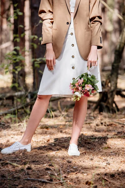 Vista recortada de la novia en chaqueta marrón celebración de ramo de boda en el bosque - foto de stock
