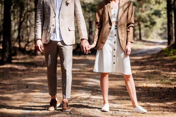 Visão cortada de casal na moda de mãos dadas na floresta — Fotografia de Stock