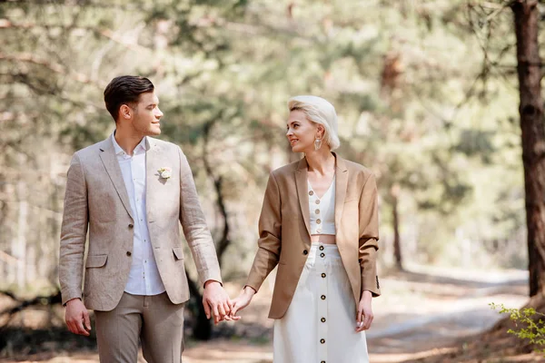 Glückliches stilvolles Paar hält Händchen und schaut sich im Wald an — Stockfoto
