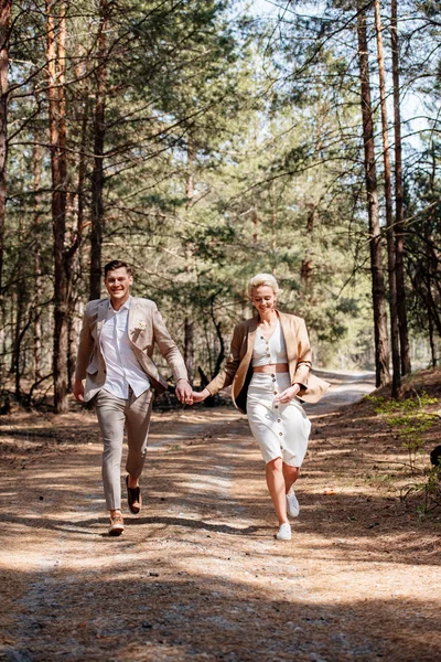 Vista completa de pareja recién casada cogida de la mano y caminando en el bosque - foto de stock