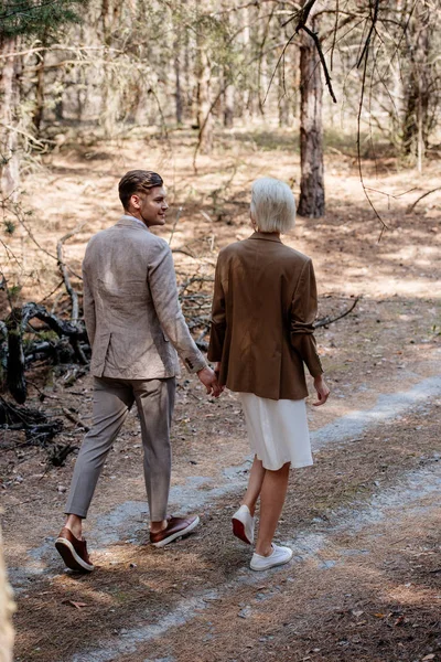 Vista a tutta lunghezza di coppia elegante che si tiene per mano e cammina nella foresta — Foto stock