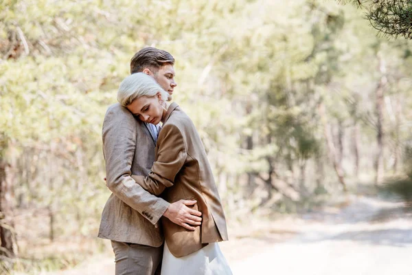 Stylish couple in elegant jackets embracing in forest — Stock Photo