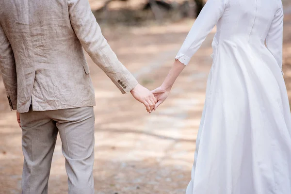 Vista recortada de pareja recién casada cogida de la mano en el bosque - foto de stock