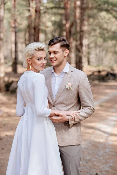 Just married couple in formal wear embracing in forest — Stock Photo