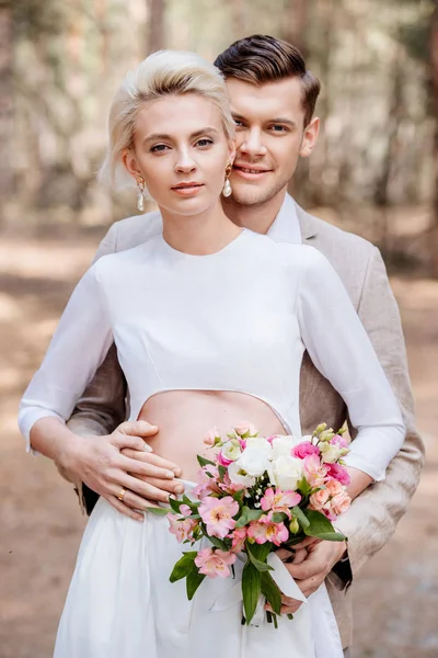 Couple marié souriant avec bouquet de mariage embrassant dans la forêt — Photo de stock