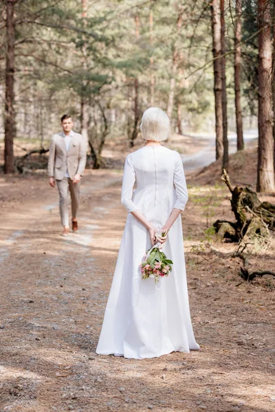 Rückansicht Braut mit Blumen und Bräutigam im Wald — Stockfoto