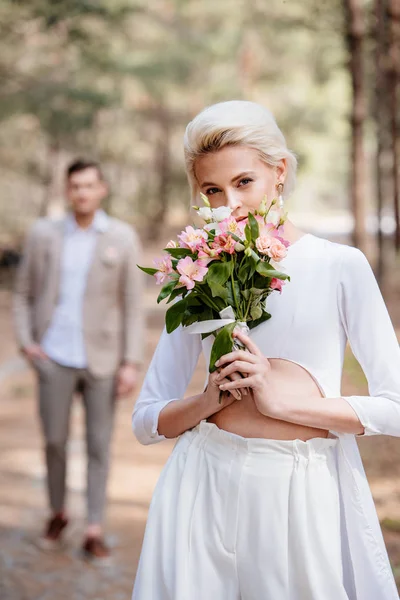 Hübsche Braut mit Blumenstrauß und Bräutigam im Wald — Stockfoto