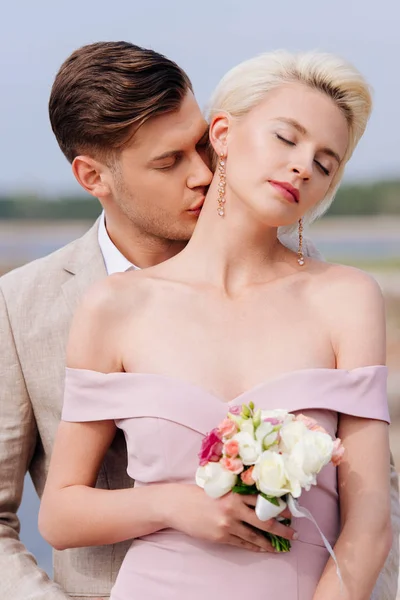 Noivo elegante beijando noiva no pescoço com os olhos fechados — Fotografia de Stock