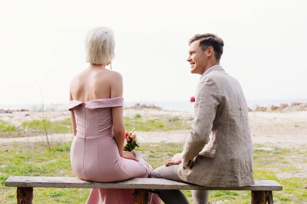 Mariée avec bouquet et marié assis sur le banc — Photo de stock