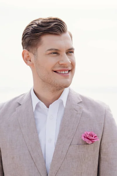 Elegante novio sonriente en ropa formal con boutonniere mirando hacia otro lado - foto de stock