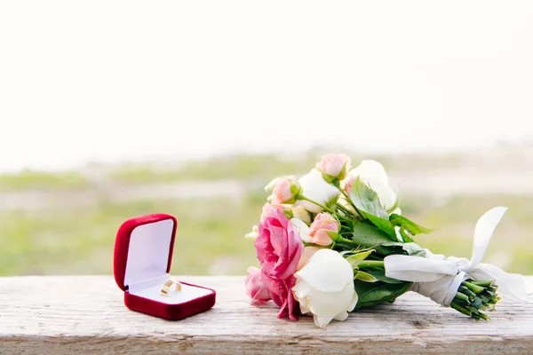 Wedding ring in red box and bouquet on wooden surface — Stock Photo