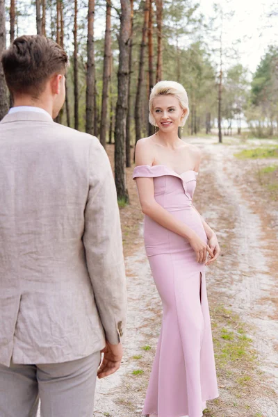 Lächelndes Mädchen in rosa Kleid schaut Bräutigam im Wald an — Stockfoto