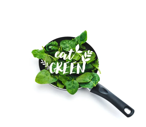 Folhas de espinafre fresco na frigideira com comer letras verdes no fundo branco — Fotografia de Stock
