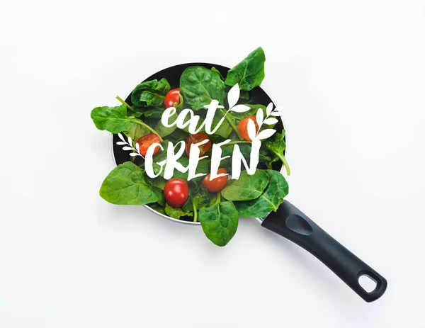 Folhas de espinafre frescas e tomates cereja na frigideira com comer letras verdes no fundo branco — Fotografia de Stock
