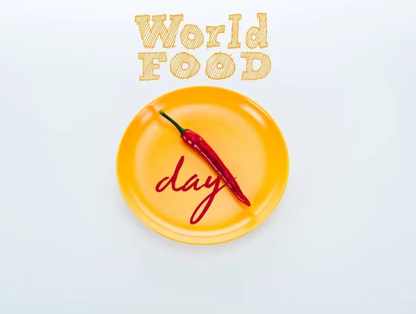 Top view of red chili pepper on bright yellow plate with world food day lettering on white background — Stock Photo