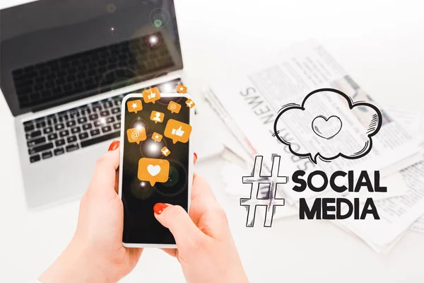 Selektiver Fokus der Frau mit Smartphone und Social-Media-Symbolen in der Nähe von Laptop und Zeitungen — Stockfoto