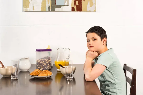 Мальчик-подросток сидит за столом во время завтрака и смотрит в камеру — стоковое фото
