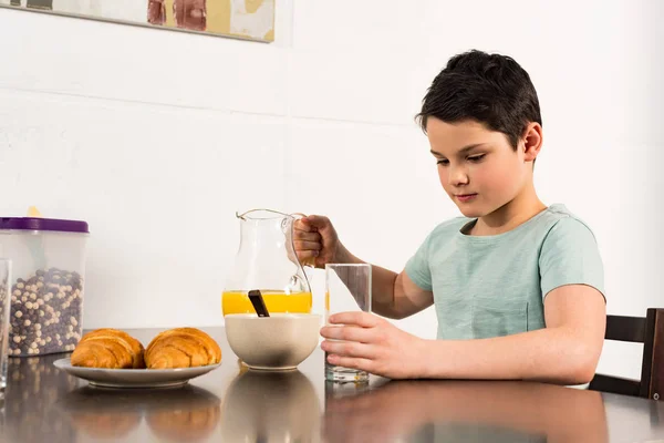 Мальчик держит стекло и кувшин с апельсиновым соком на кухне — стоковое фото