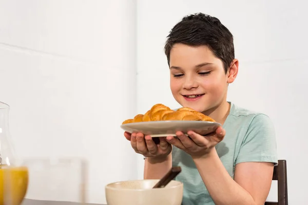 Smiling preteen boy holding plate with croissants in kitchen — Stock Photo