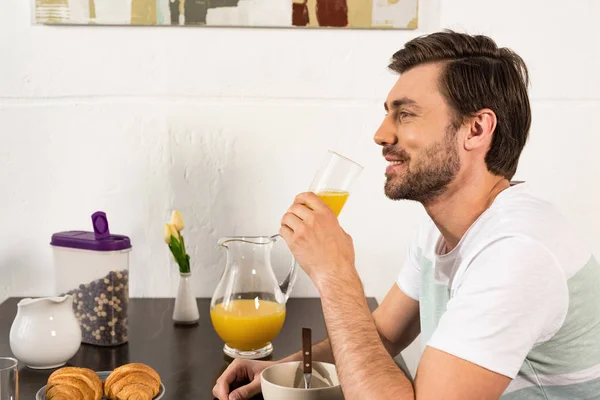 Homem barbudo sorrindo segurando vidro de suco de laranja durante o café da manhã — Fotografia de Stock