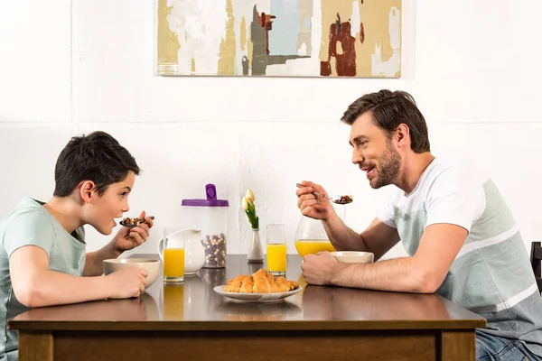 Smiling father and son having breakfast and looking at each other in kitchen — Stock Photo