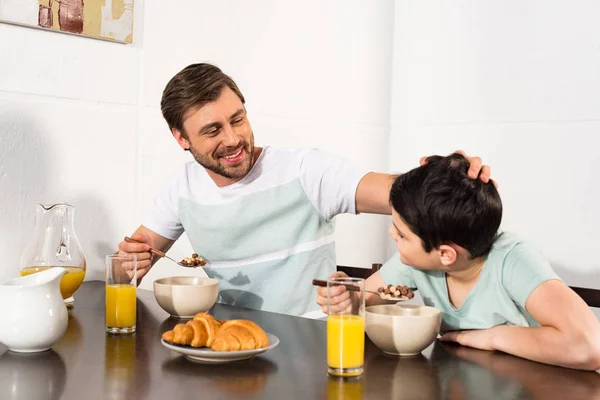 Souriant père caressant fils pendant le petit déjeuner dans la cuisine — Photo de stock