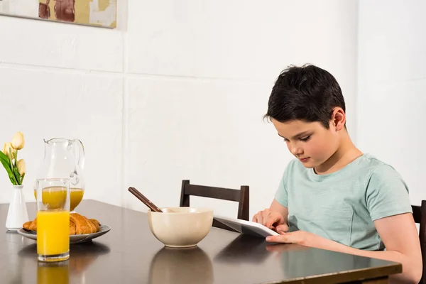Garçon utilisant tablette numérique pendant le petit déjeuner dans la cuisine — Photo de stock