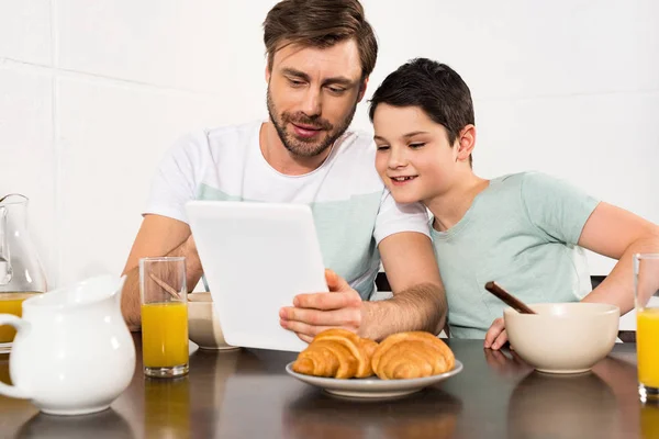 Smiling dad and son using digital tablet during breakfast — Stock Photo