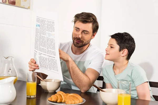 Papà e figlio leggono il giornale durante la colazione in cucina — Foto stock