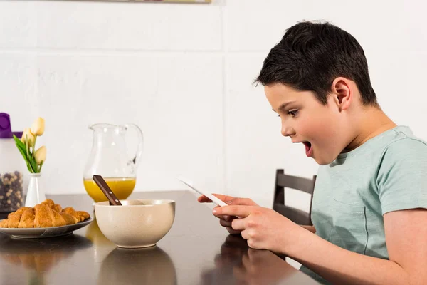 Choqué garçon en utilisant tablette numérique pendant le petit déjeuner dans la cuisine — Photo de stock