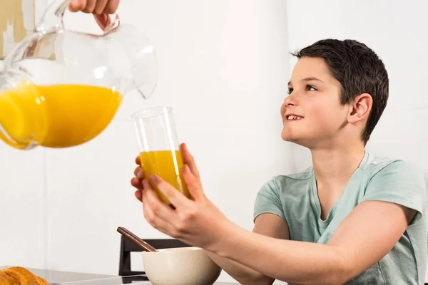 Обрізаний вид батька, що поливає апельсиновий сік синові на кухні — стокове фото