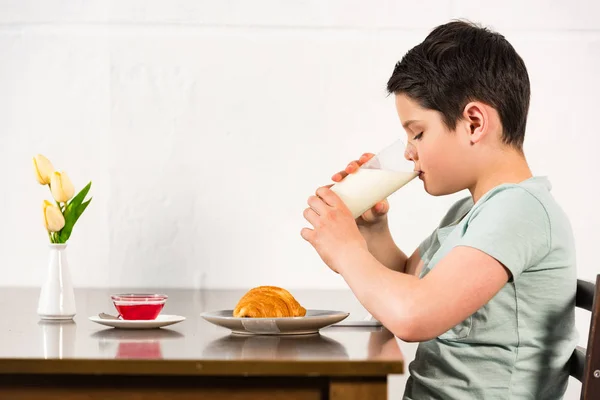 Vista lateral del niño bebiendo leche durante el desayuno - foto de stock