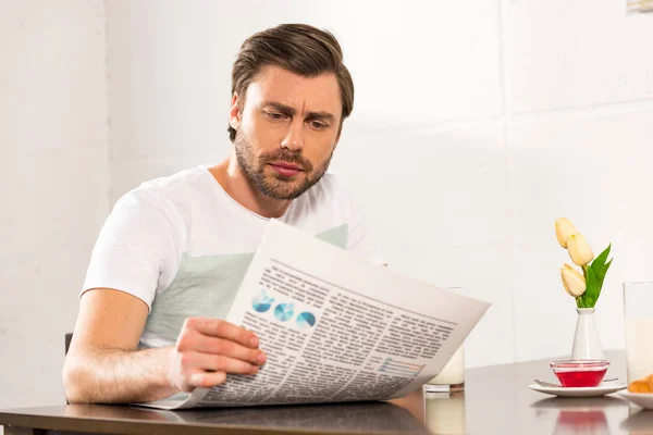Зосереджений бородатий чоловік читає газету під час сніданку на кухні — стокове фото
