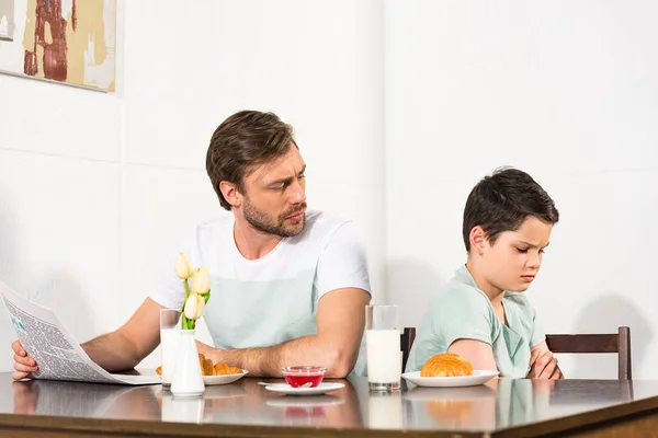 Father with newspaper looking at offended son during breakfast — Stock Photo