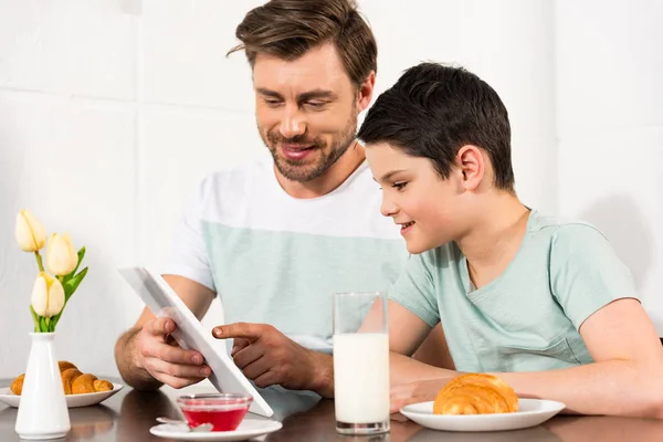 Sonriente padre e hijo usando tableta digital durante el desayuno - foto de stock