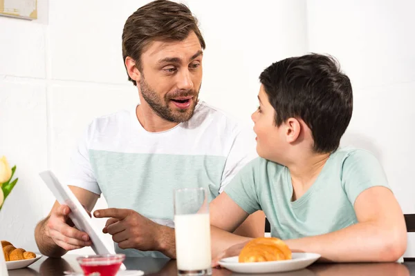 Pai surpreso e filho usando tablet digital durante o café da manhã — Fotografia de Stock